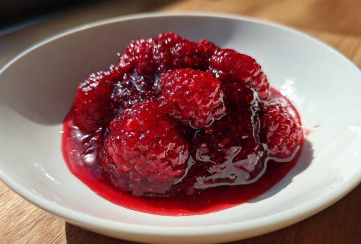 Close-up of chunky, vibrant red raspberry jam with whole berries in a white bowl.