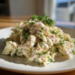 A mound of creamy cottage cheese chicken salad mixed with red onion and fresh dill, served on a white plate.