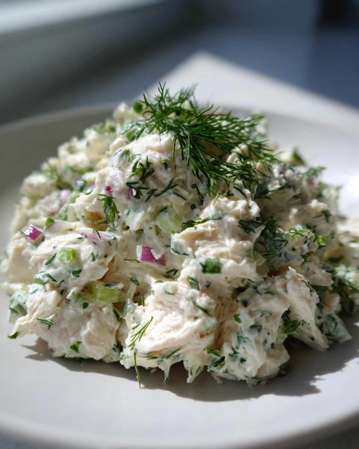 Close-up of creamy cottage cheese chicken salad mixed with red onion and celery, topped with fresh dill.