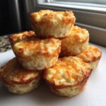 A stack of six golden brown cottage cheese egg cups topped with melted cheddar cheese.