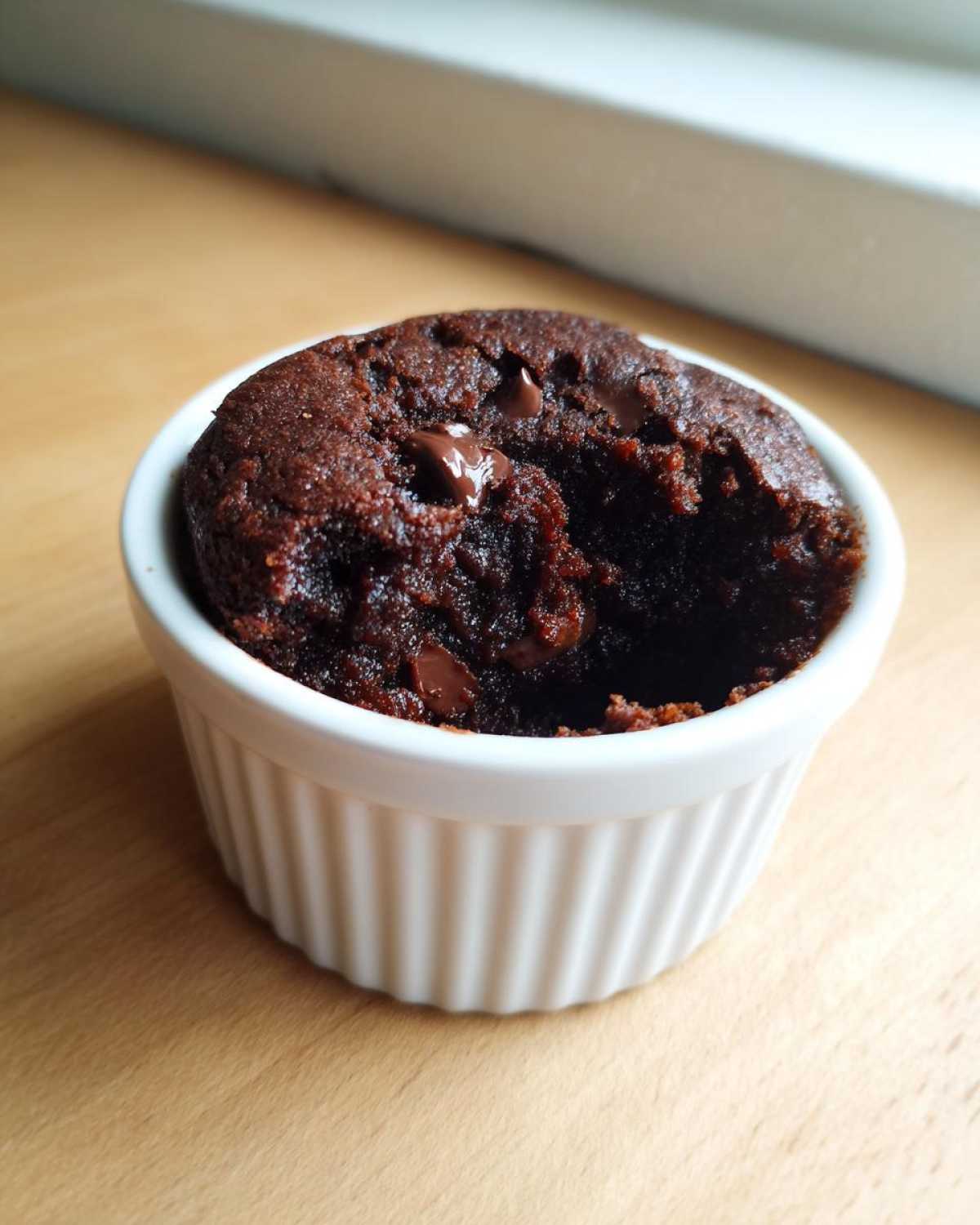 Close-up of a dark, fudgy Cottage Cheese Microwave Brownie topped with melted chocolate chips in a white ramekin.