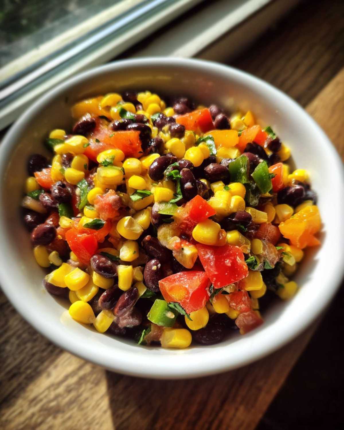 Close-up of vibrant cowboy caviar featuring black beans, corn, diced tomatoes, and peppers in a white bowl.