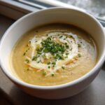 A close-up of a bowl of creamy cauliflower soup, swirled with cream and topped with fresh chopped chives.