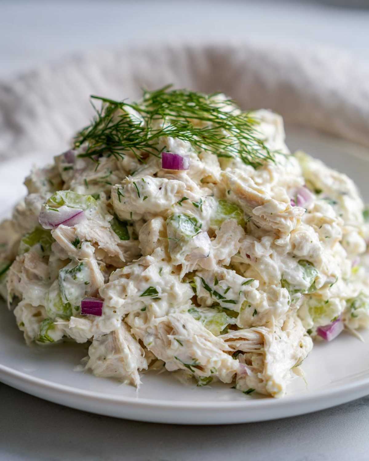 A mound of creamy cottage cheese chicken salad mixed with celery and red onion, topped with fresh dill.