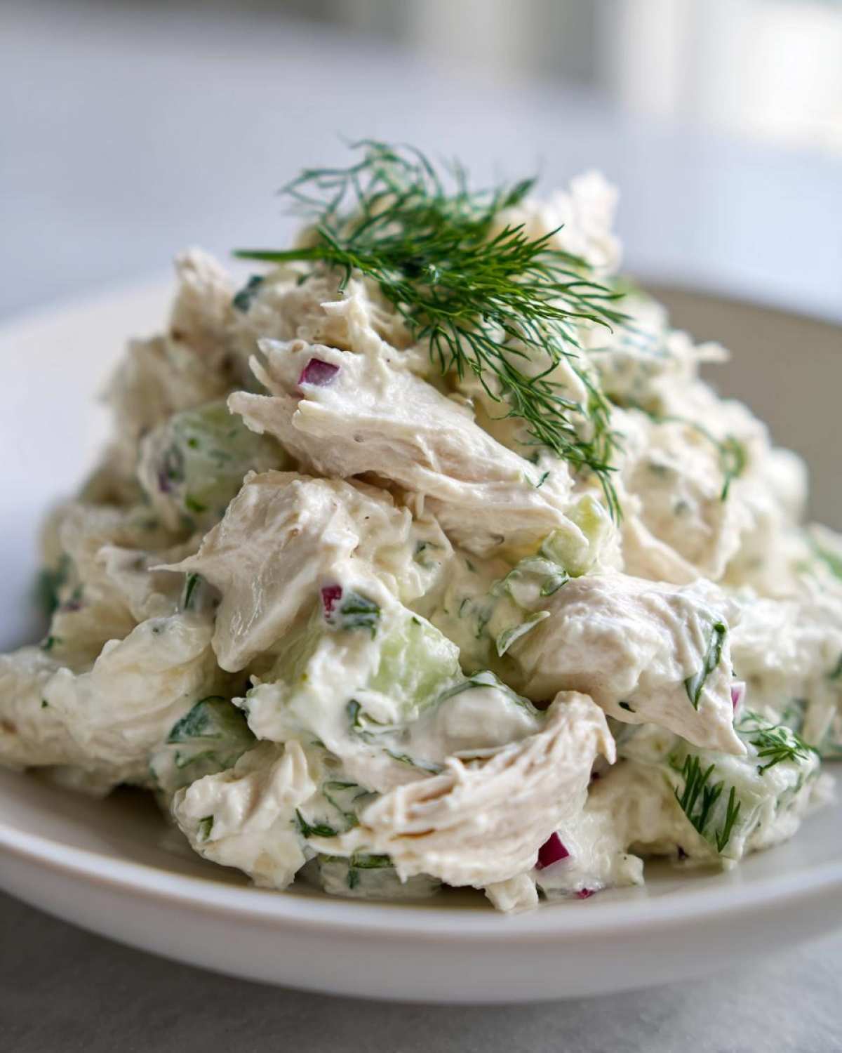 Close-up of a serving of creamy cottage cheese chicken salad mixed with celery and red onion, topped with fresh dill.