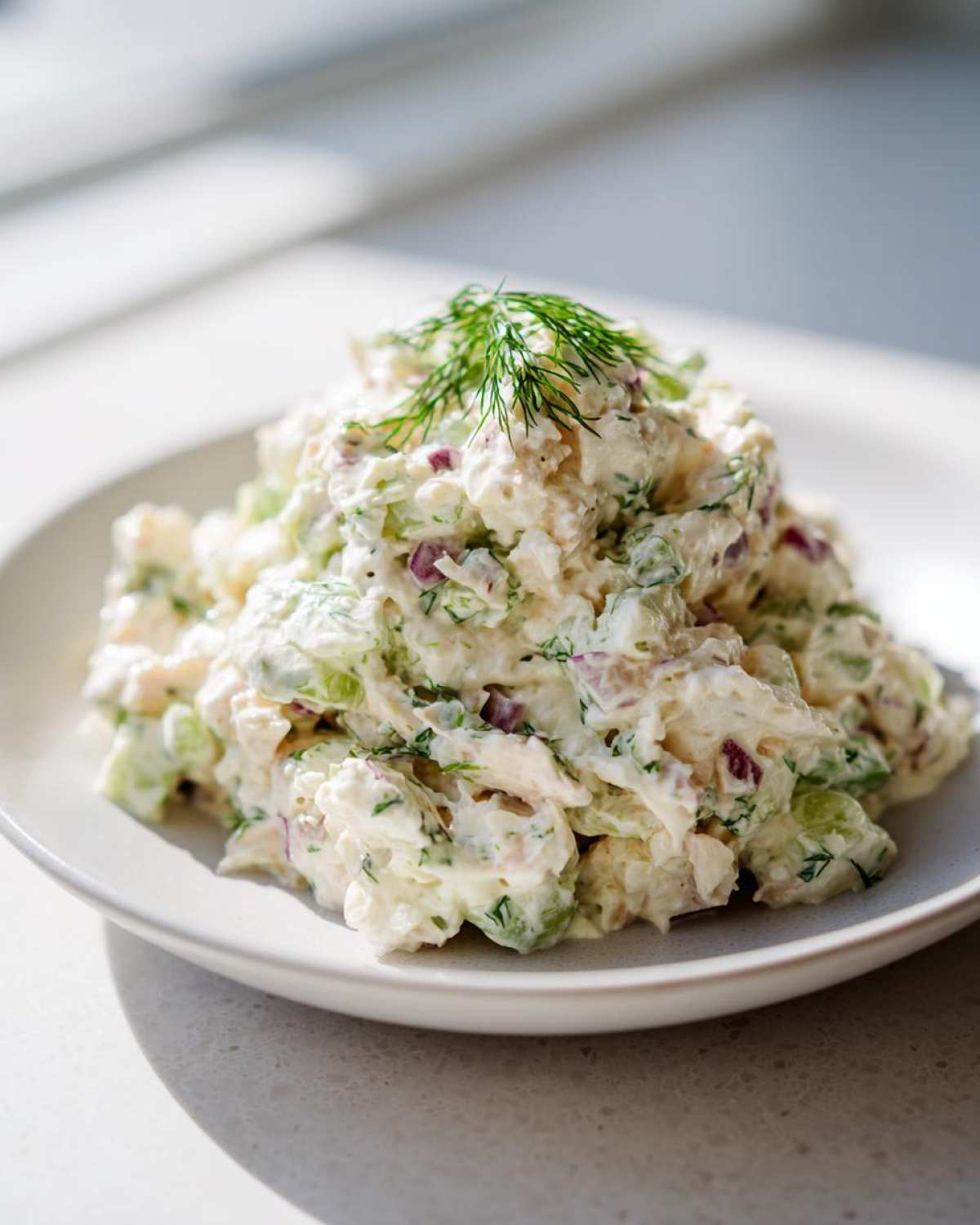 A mound of creamy cottage cheese chicken salad mixed with celery and red onion, topped with fresh dill.