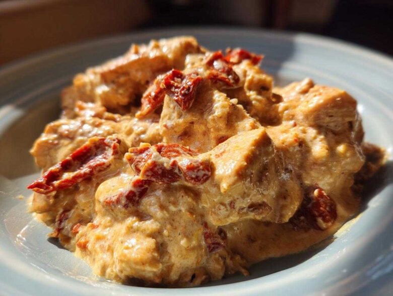 Close-up of creamy crockpot marry me chicken chunks topped with vibrant sun-dried tomatoes.