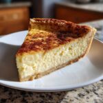 A thick slice of creamy custard pie with a golden-brown, cinnamon-dusted top, resting on a white plate.
