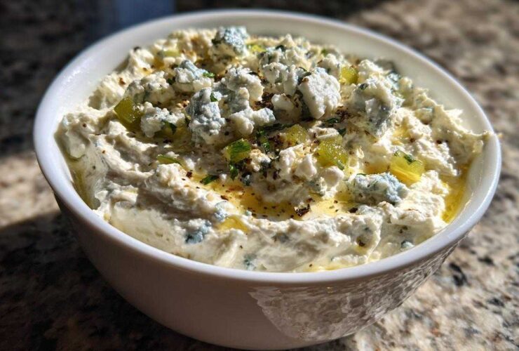 Close-up of a white bowl filled with creamy dirty martini dip topped with blue cheese crumbles and olive pieces.