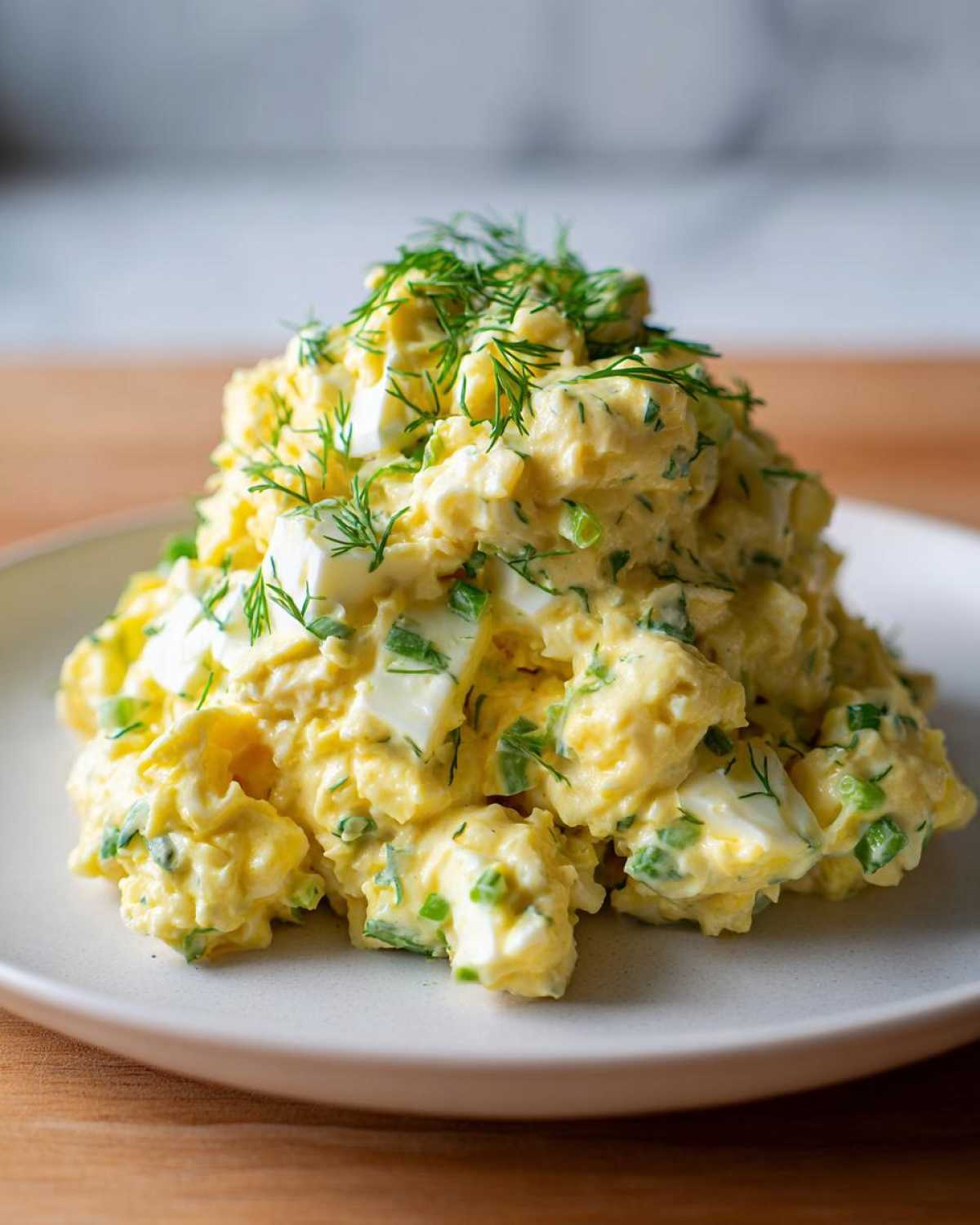 A generous mound of creamy egg salad recipe, featuring visible chunks of egg white and topped with fresh dill.
