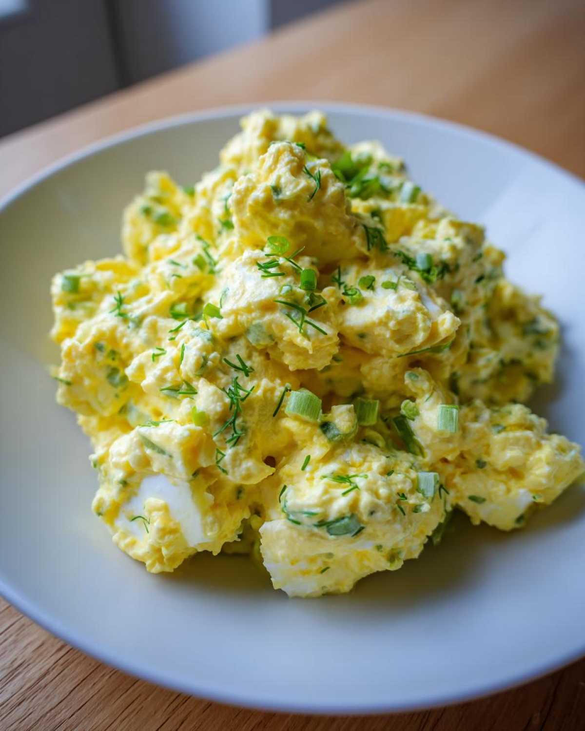 A close-up of creamy, yellow egg salad recipe garnished generously with chopped green onions and dill.