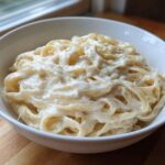 A white bowl filled with fettuccine pasta generously coated in rich, creamy homemade alfredo sauce.