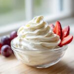 A swirl of creamy white fruit dip garnished with sliced strawberries and grapes nearby.