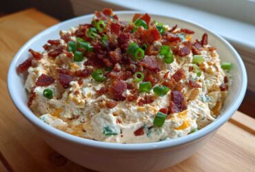 A white bowl filled with creamy Million Dollar Dip, topped generously with crumbled bacon and sliced green onions.