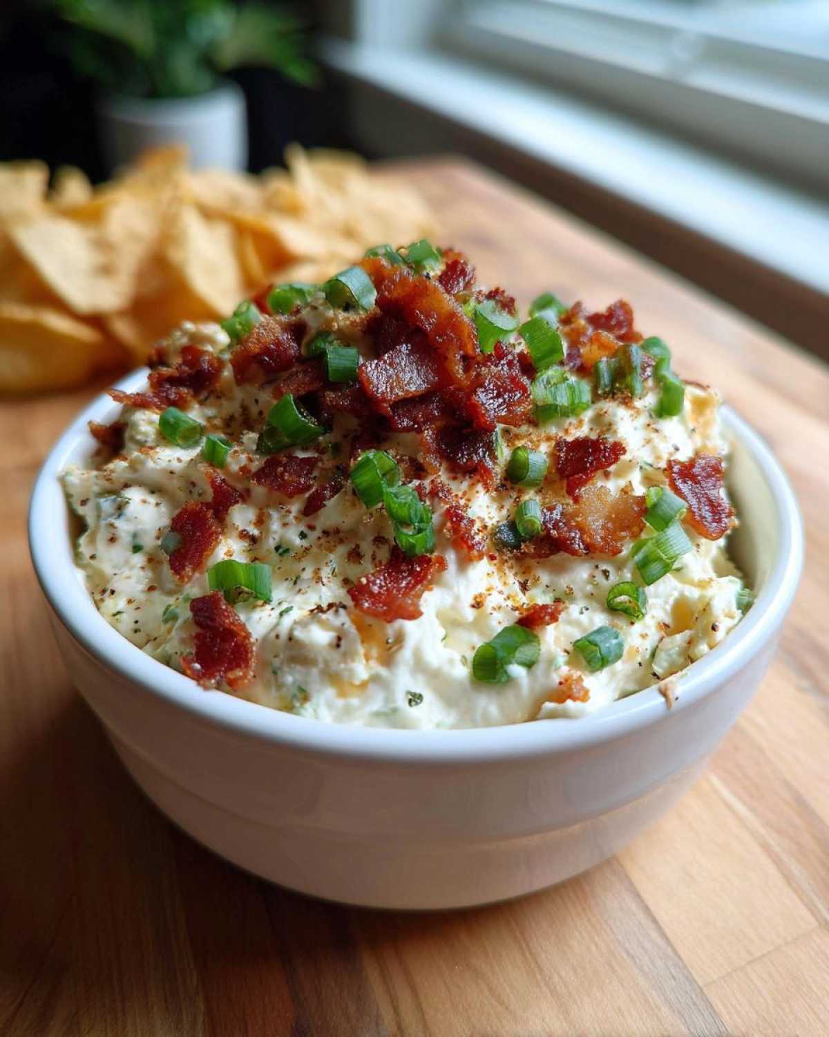 Close-up of a bowl of creamy Million Dollar Dip topped generously with crumbled bacon and sliced green onions.