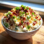 A creamy bowl of Million Dollar Dip generously topped with crumbled bacon and fresh green onions.