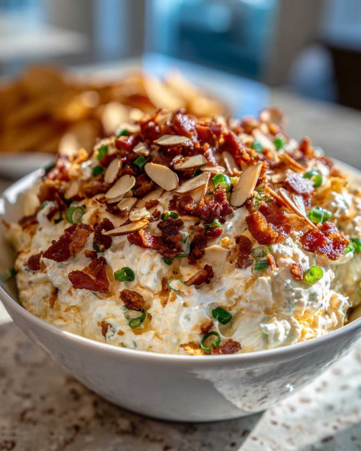 A close-up of creamy Neiman Marcus dip garnished generously with crumbled bacon, sliced almonds, and green onions.