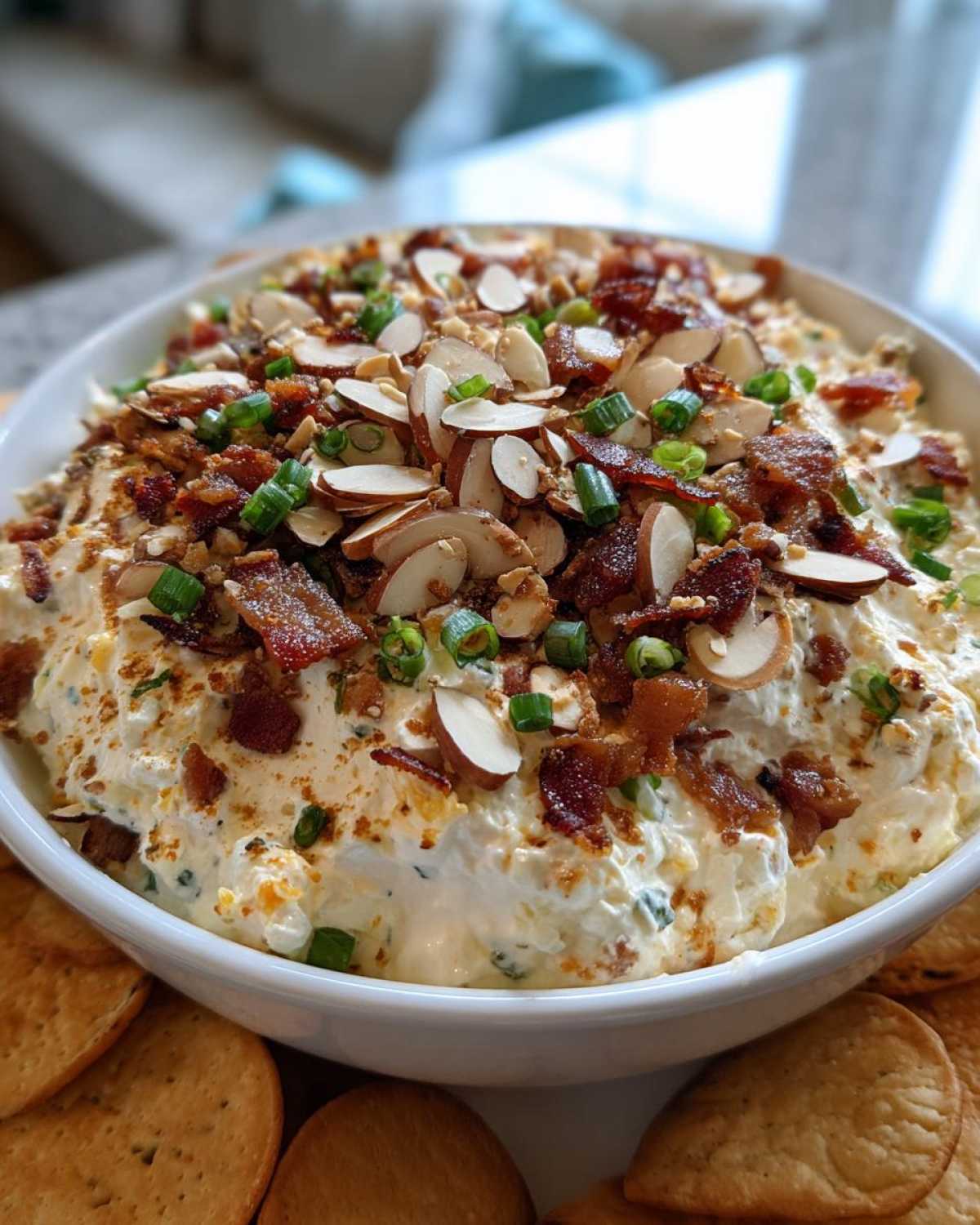 A close-up of the creamy Neiman Marcus dip served in a white bowl, generously topped with bacon bits, sliced almonds, and green onions.