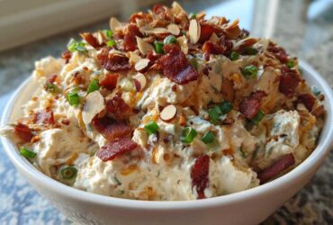 A white bowl filled with creamy Neiman Marcus dip, topped generously with crumbled bacon, sliced almonds, and green onions.