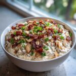 A creamy bowl of Neiman Marcus dip topped generously with bacon bits, sliced almonds, and green onions.