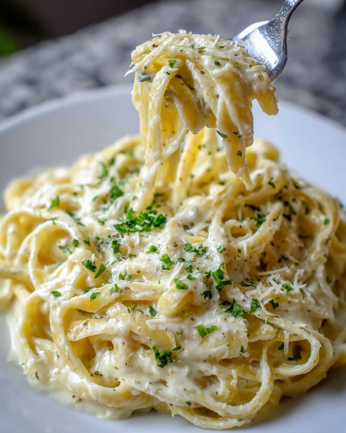 Close-up of fettuccine pasta coated in creamy Olive Garden Alfredo Sauce, lifted by a fork.