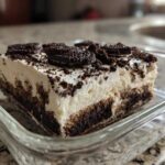 A close-up view of a generous slice of creamy oreo dirt cake topped with crushed cookies.