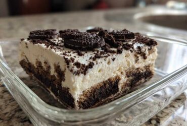 A close-up view of a generous slice of creamy oreo dirt cake topped with crushed cookies.