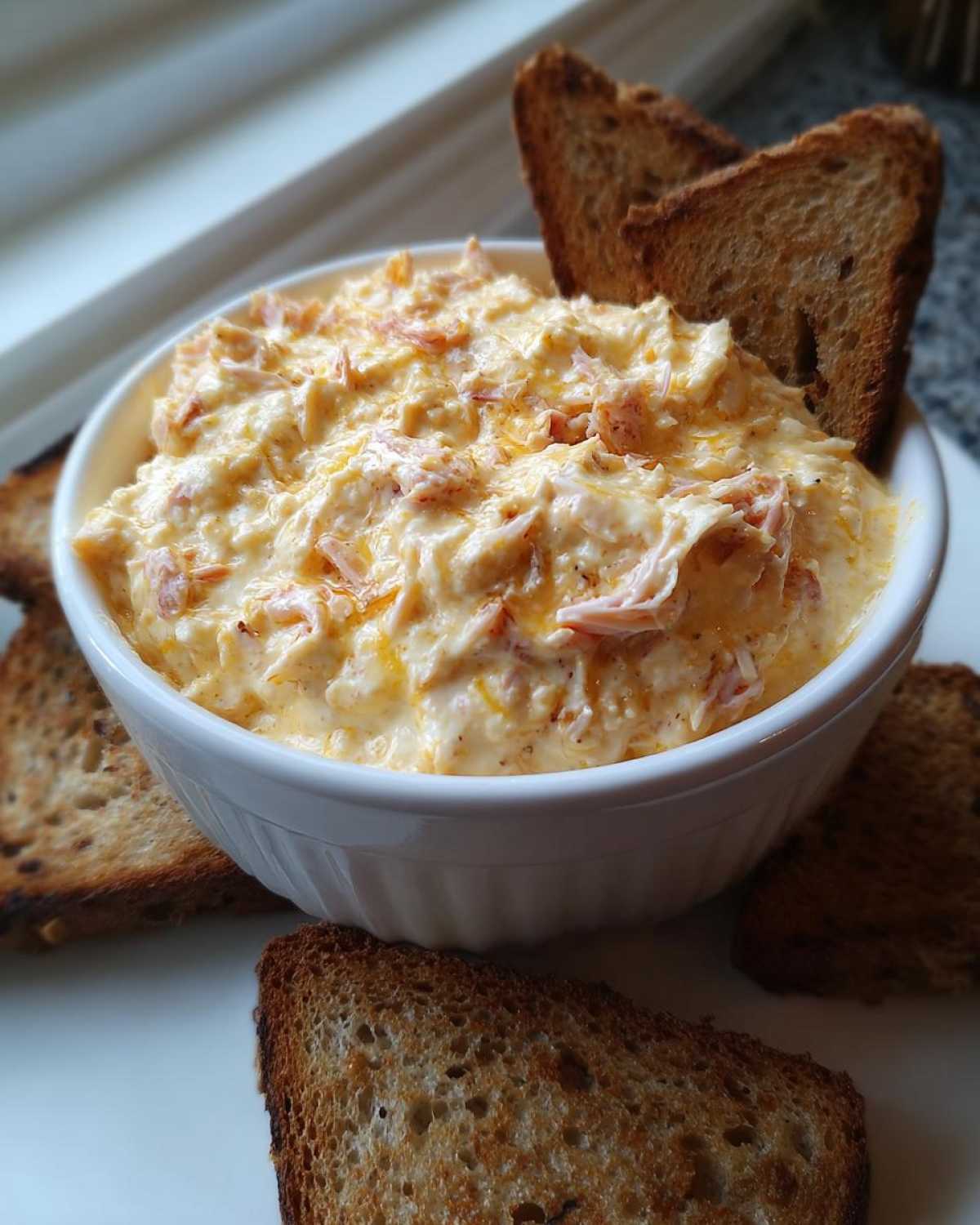 A white bowl filled with creamy, cheesy reuben dip, surrounded by toasted rye bread pieces for dipping.