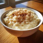 A close-up of a white bowl filled with creamy rice pudding topped generously with ground cinnamon.