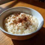 A close-up of a bowl of creamy rice pudding sprinkled generously with cinnamon.