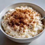 A close-up of a bowl of creamy rice pudding recipe generously dusted with ground cinnamon.