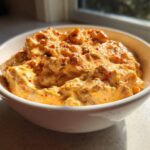 A close-up of creamy, cheesy rotel dip topped with red pepper flakes in a white serving bowl.