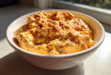 A close-up of creamy, cheesy rotel dip topped with red pepper flakes in a white serving bowl.