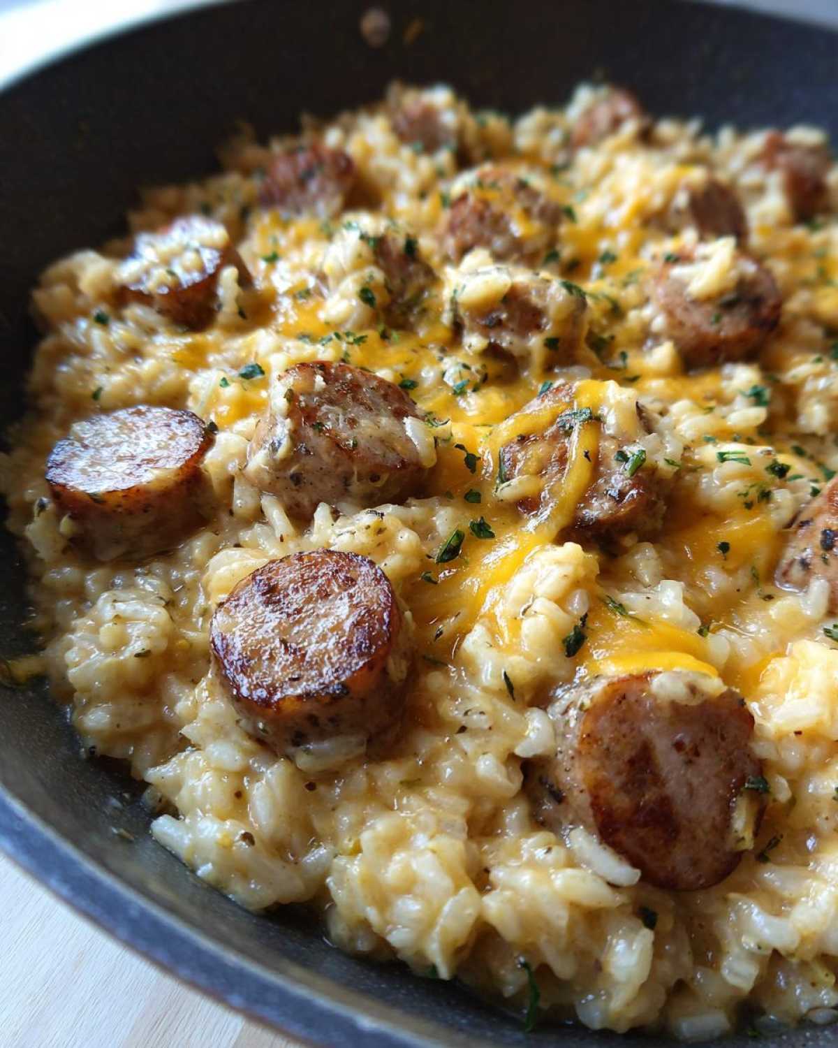 Close-up of creamy sausage and rice mixed with melted cheddar cheese and sprinkled with parsley in a skillet.
