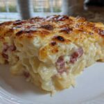 A close-up of a rich, creamy slice of scalloped potatoes and ham with a golden-brown, cheesy top.