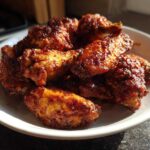 A close-up of several golden brown, saucy crispy baked chicken wings piled high on a white dish.