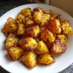 A close-up of golden, crispy breakfast potatoes seasoned with herbs served on a white plate.