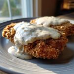 Two pieces of crispy, golden brown chicken fried steak smothered in creamy, black pepper-flecked country gravy.