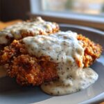 Close-up of two pieces of crispy chicken fried steak smothered in thick, creamy white pepper gravy.