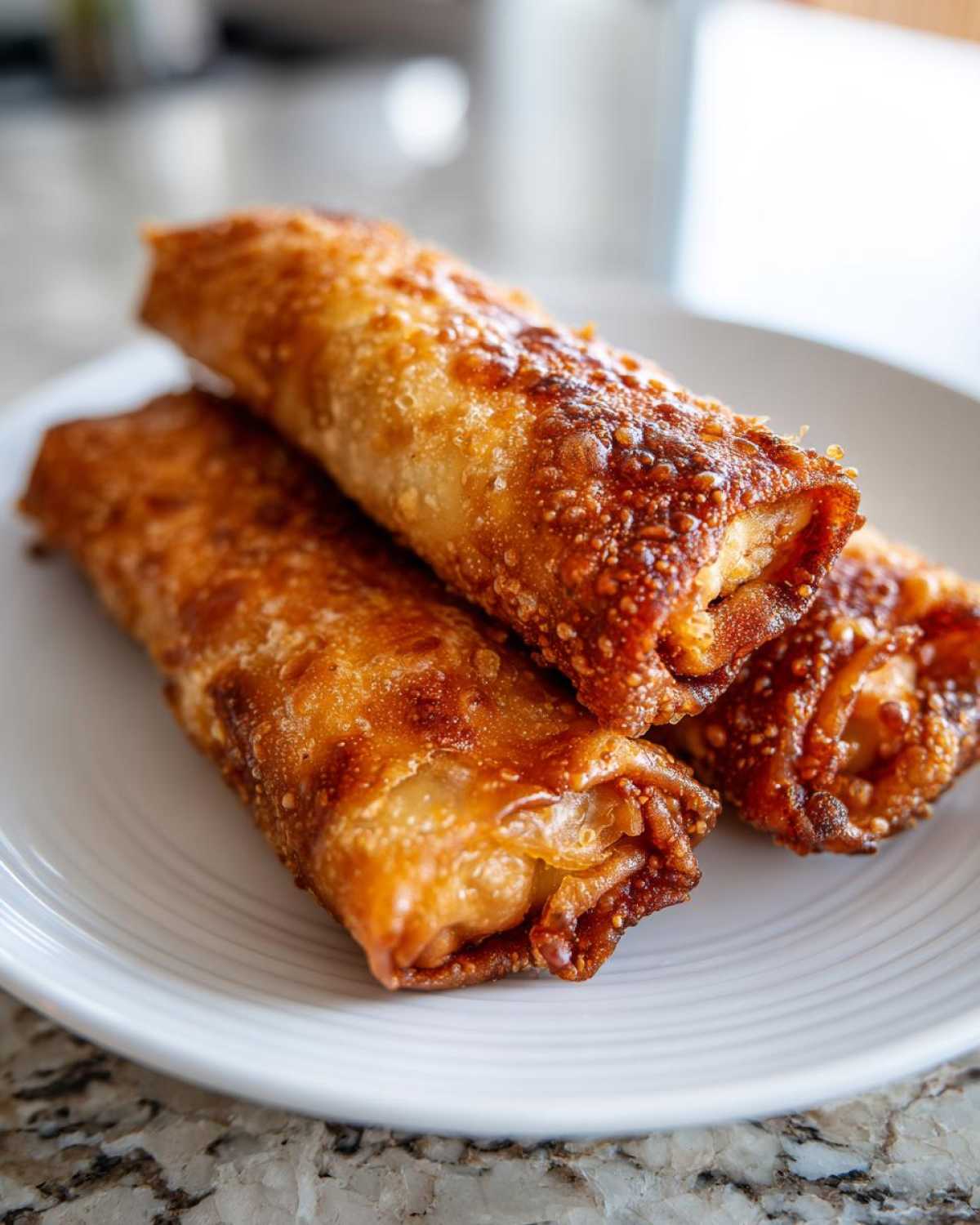 Close-up of three golden brown, crispy egg roll appetizers stacked on a white plate.