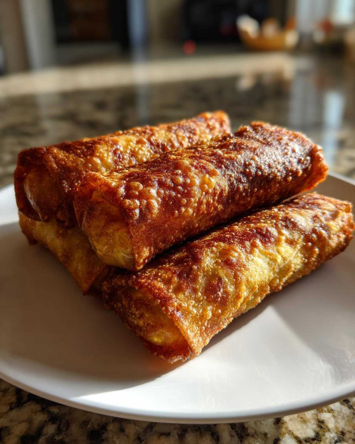 Four perfectly cooked, golden brown, crispy egg roll appetizers stacked on a white plate.