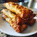 A stack of golden brown, crispy fried egg roll appetizers piled high on a white plate.