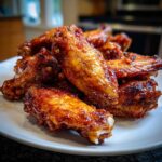 Close-up of a pile of perfectly glazed, crispy chicken wings on a white plate.