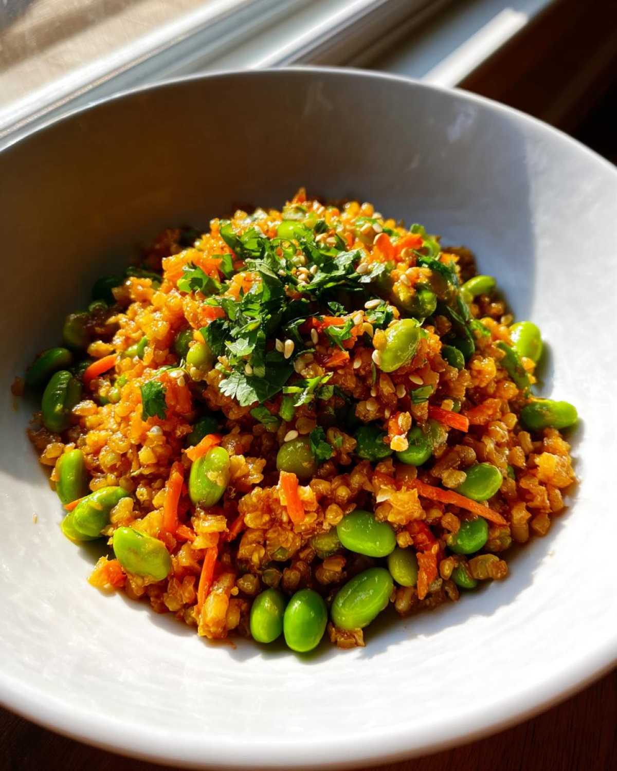 A vibrant bowl of crispy rice salad mixed with bright green edamame, shredded carrots, and topped with cilantro.