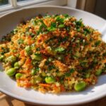 A close-up of a vibrant crispy rice salad topped with toasted breadcrumbs, edamame, shredded carrots, and fresh parsley.