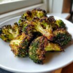 Close-up of perfectly crisp roasted broccoli florets with dark, caramelized edges served on a white plate.
