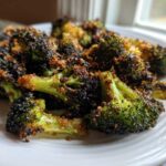 Close-up of perfectly roasted broccoli with crispy, browned edges served on a white plate.