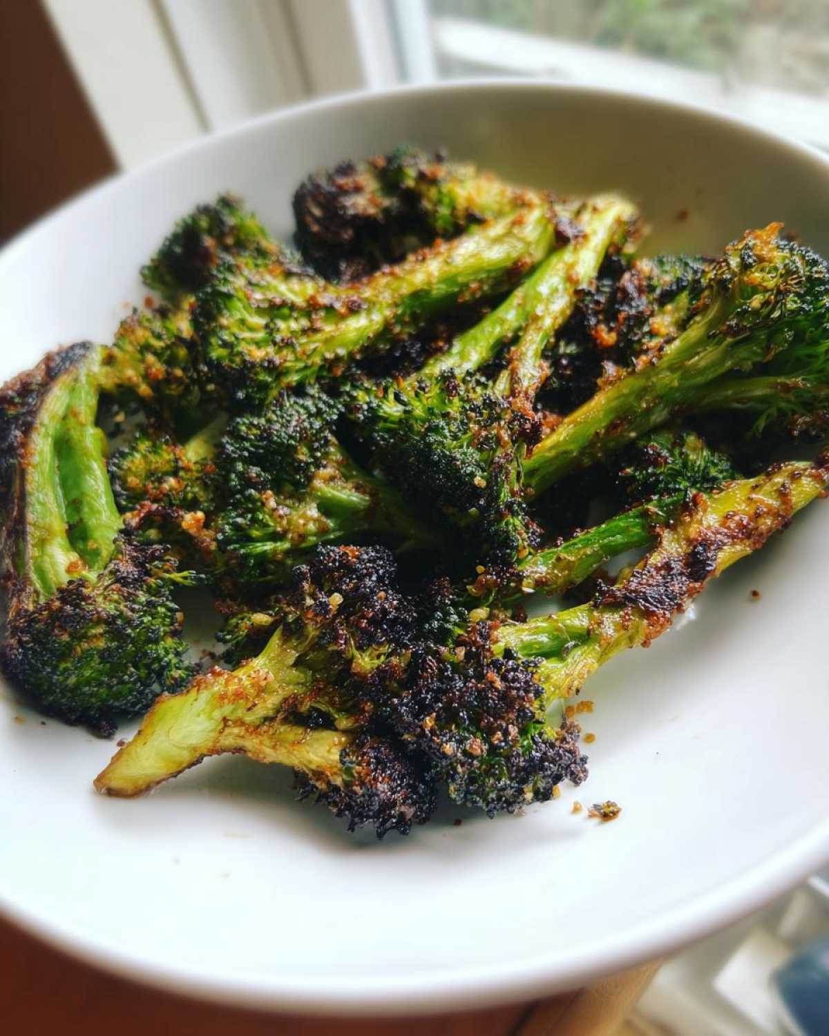 Close-up of perfectly crisp, slightly charred roasted broccoli florets seasoned and served in a white bowl.