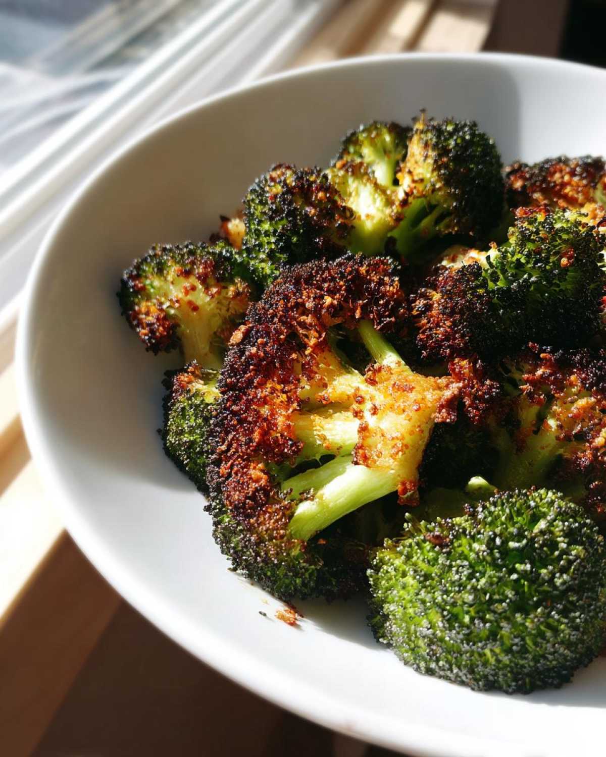 Close-up of perfectly crispy roasted broccoli florets with dark, caramelized edges served in a white bowl.