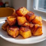 A pile of golden brown, caramelized roasted sweet potato cubes stacked on a white plate.
